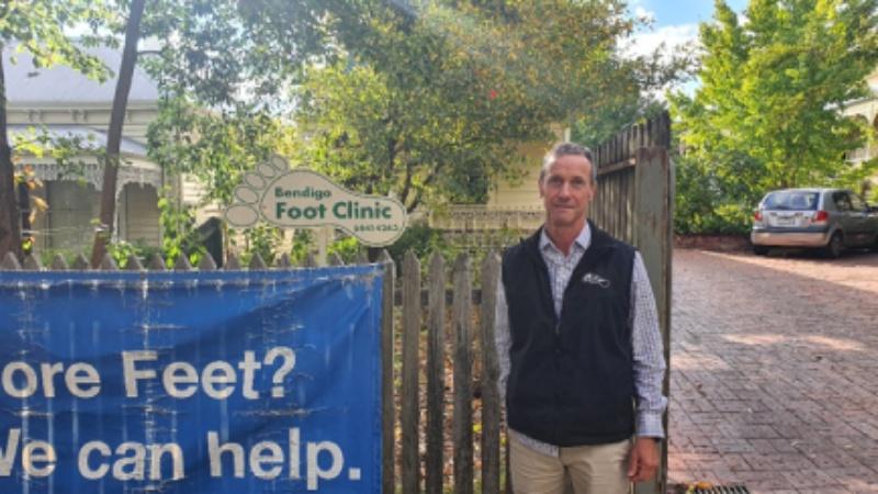 Owner of Bendigo Foot Clinic standing in front of entrance sign.