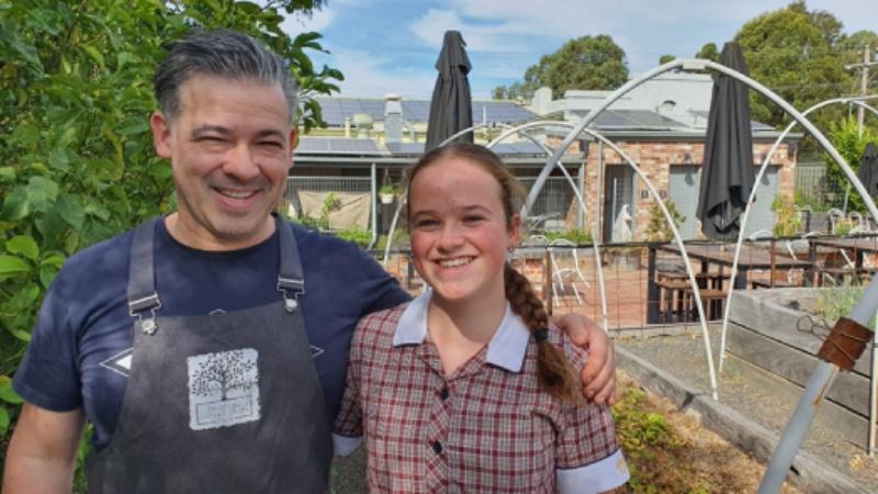 Owner of Spring Gully General Store standing beside girl in courtyard area.