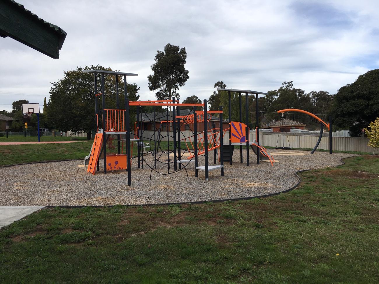 An orange and purple playground with grass in front and cloudy sky behind