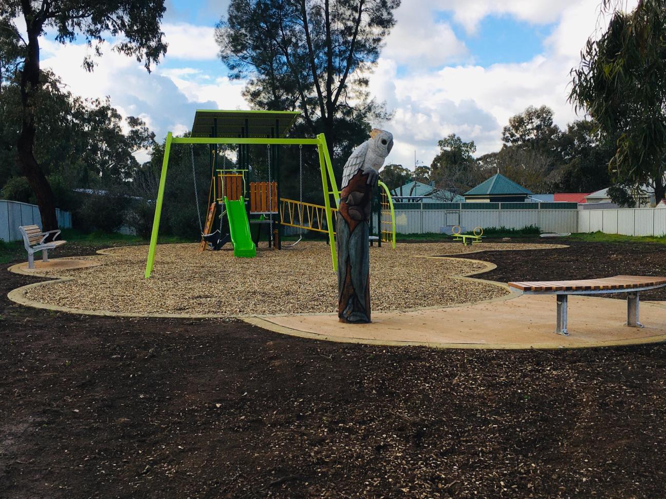 A playground with a bright green slide, a cockatoo sculpture and a seat