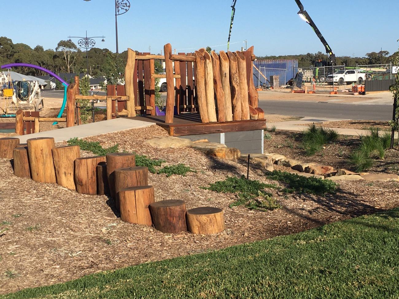 A natural timber playground with green grass in front and blue sky behind