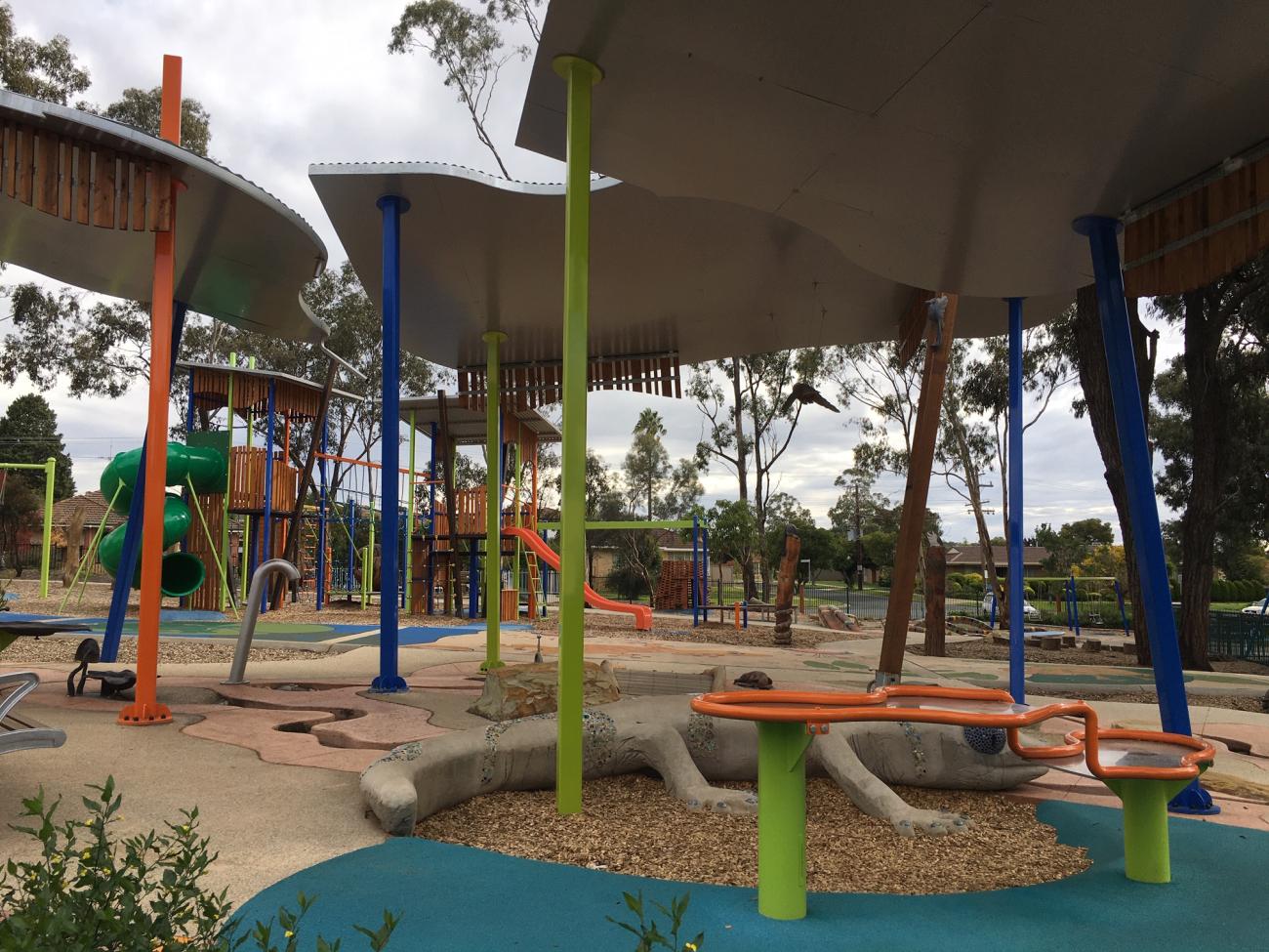 Shelters over a lizard sculpture with playground equipment in the background