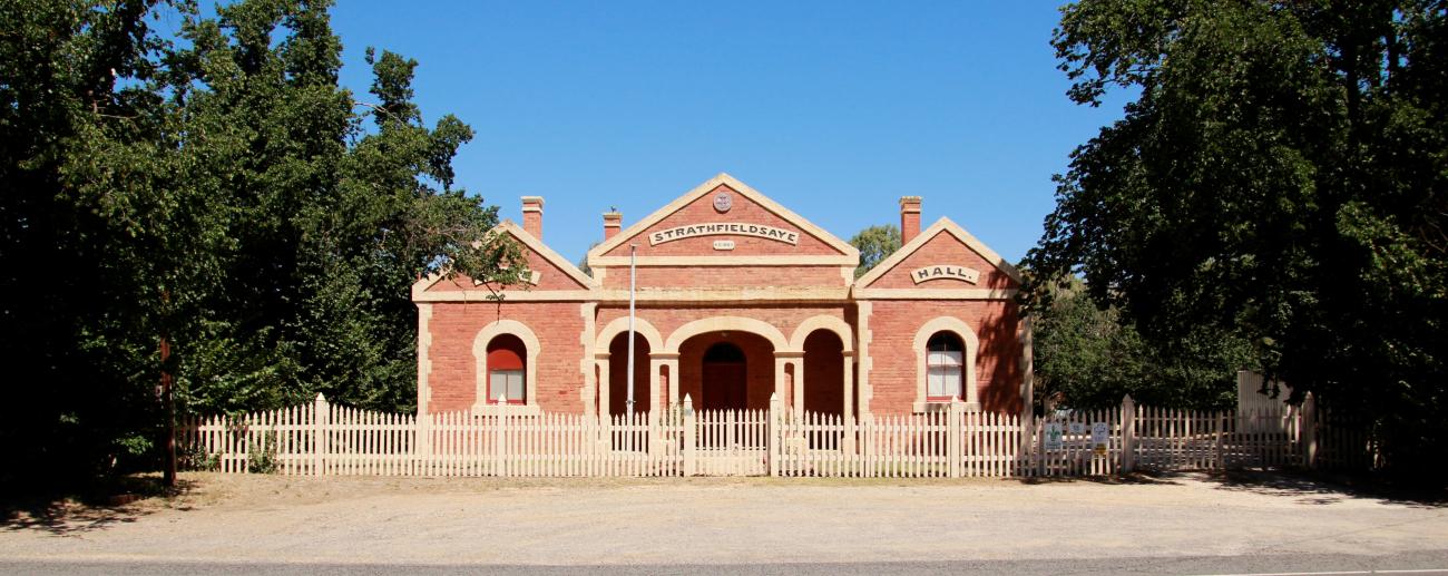 The Historic Strathfieldsaye Shire Building has a brick facade and many shady trees.