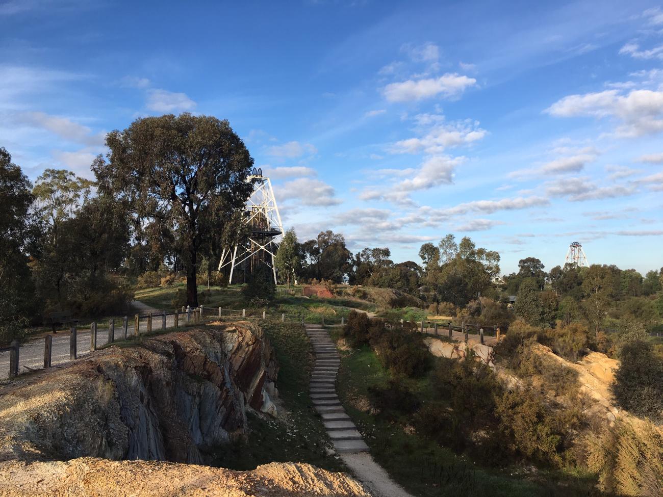 An open cut mine with a poppet head, trees and blue sky in the background