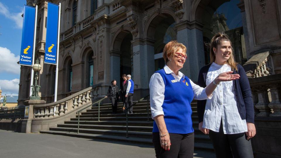Volunteer giving directions to a tourist outside a visitor information centre