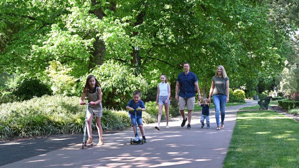 A family of six enjoy a stroll through Rosalind Park, with two children out front on scooters.