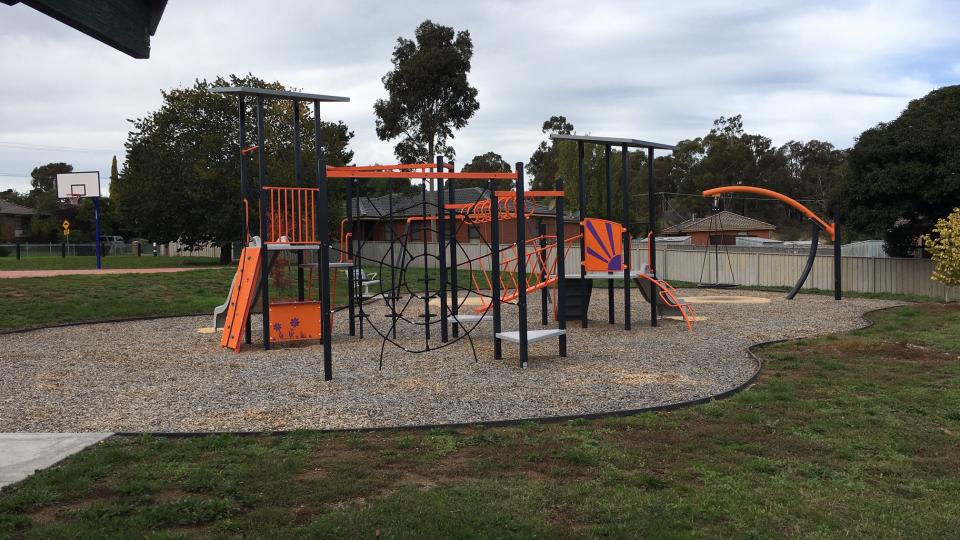 An orange and purple playground with grass in front and cloudy sky behind