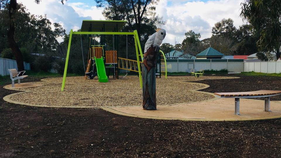 A playground with a bright green slide, a cockatoo sculpture and a seat