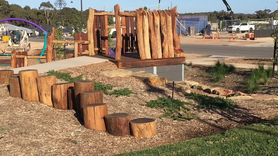 A natural timber playground with green grass in front and blue sky behind