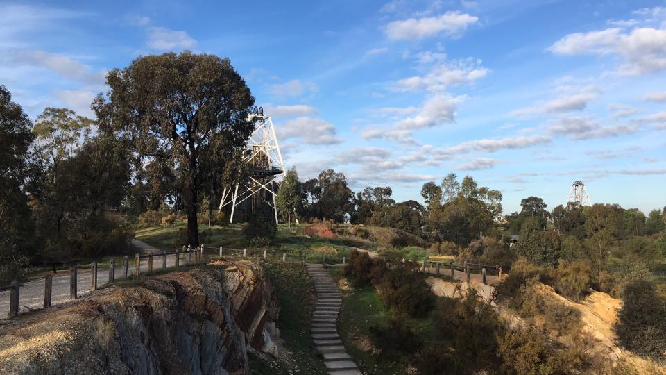 An open cut mine with a poppet head, trees and blue sky in the background